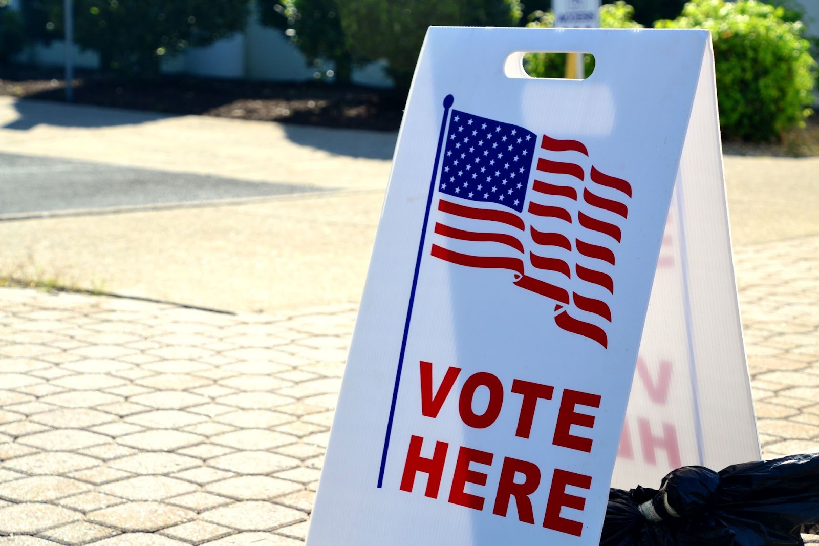 Cartel colocado en la calle con banera de Estados Unidos y texto en inglés que dice 'Vota aquí'.