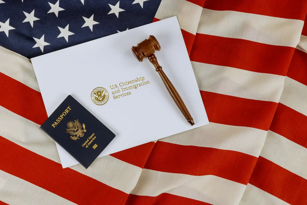 Pasaporte estadounidense y mazo sobre un sobre de USCIS y una bandera estadounidense