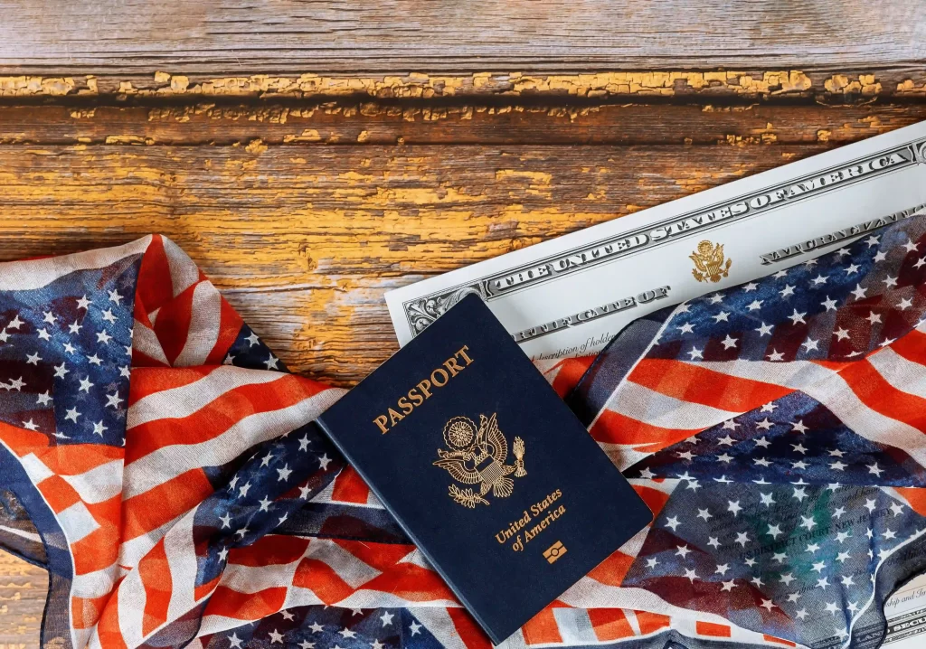 Pasaporte estadounidense sobre banderas de Estados Unidos y documento ciudadanía estadounidense encima de mesa de madera