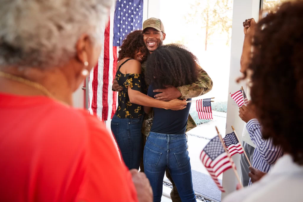 A US army soldier arriving home to his family who are waiting for him with smiles and US flags