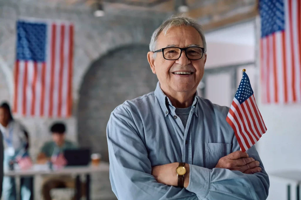 Hombre mayor sosteniendo una bandera de Estados Unidos y sonriendo