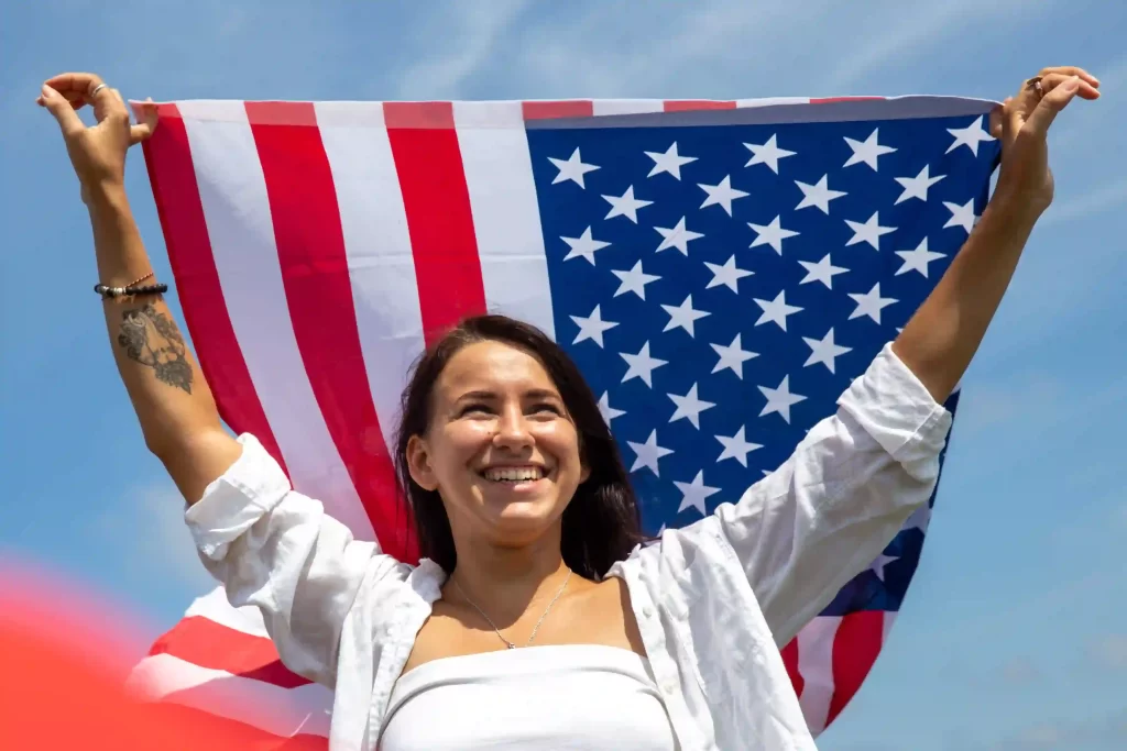 Mujer sonriendo sosteniendo una bandera de Estados Unidos sobre su cabeza