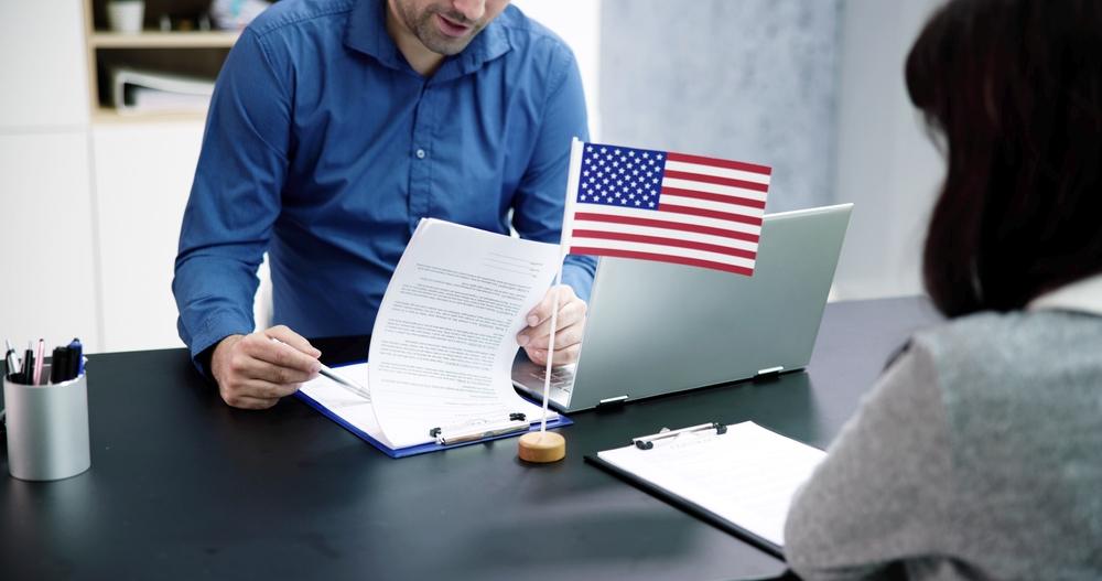 A visa applicant speaks with a consular officer during a U.S. immigration visa interview while reviewing application documents.